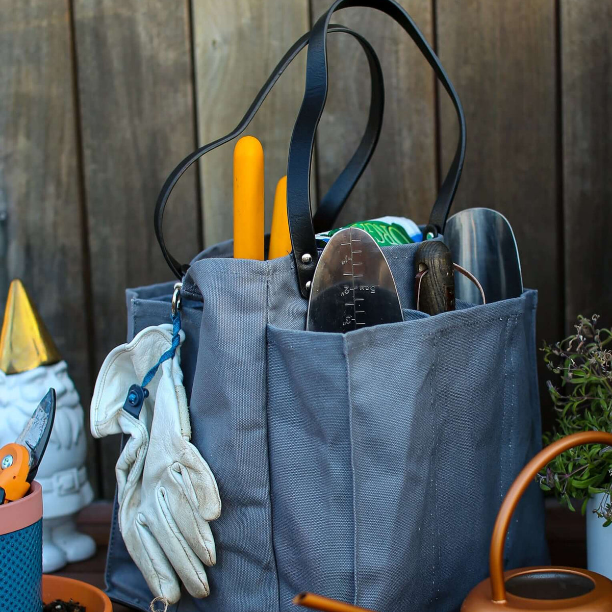 Grey multi-pocketed market tote filled with gardening tools and gloves, set on a wooden table.