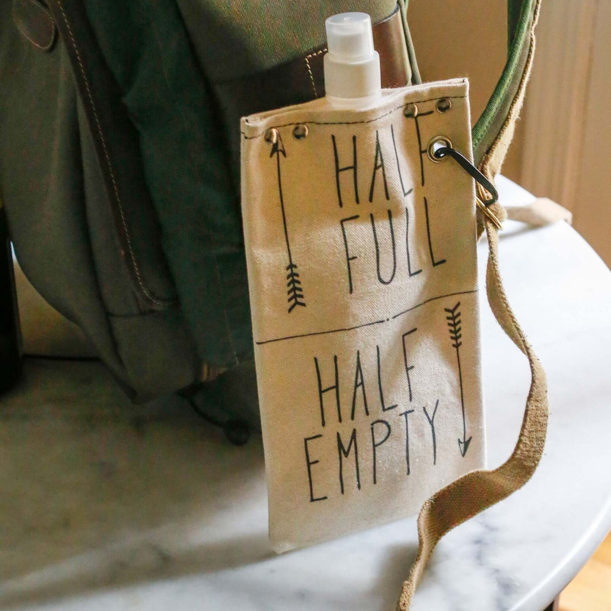 Half Full 750ml canvas canteen attached to a backpack, featuring a fun graphic design.