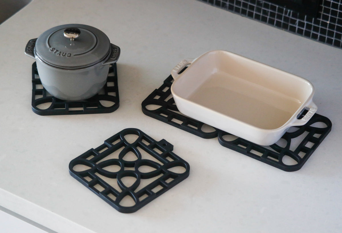Interlocking silicone trivet protecting a pot and a dish on a modern kitchen countertop.