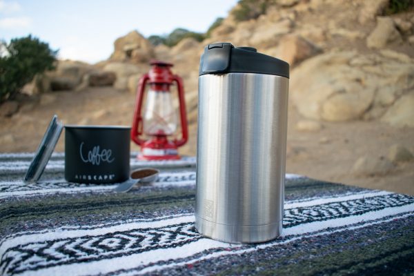 Photo of an insulated BruTreck coffee mug sitting on a covered picknick table with a lantern in the background.