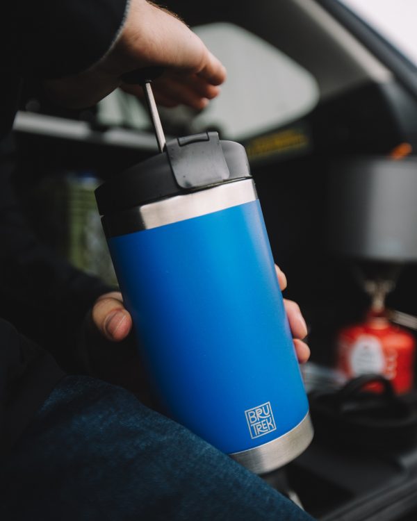 Photo of someone sitting inside a vehicle while pressing down on a blue colored coffee press plunger.