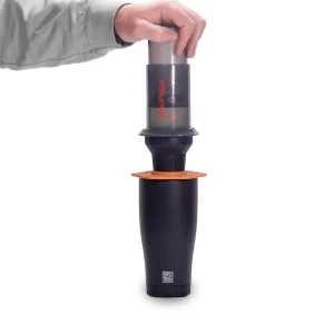 White background photo of person pressing on aeropress using Trestle adapter to make coffee into coffee tumbler