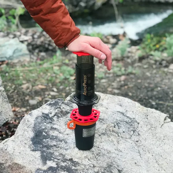 person pressing down on aeropress with trestle adapter to make coffee on rock