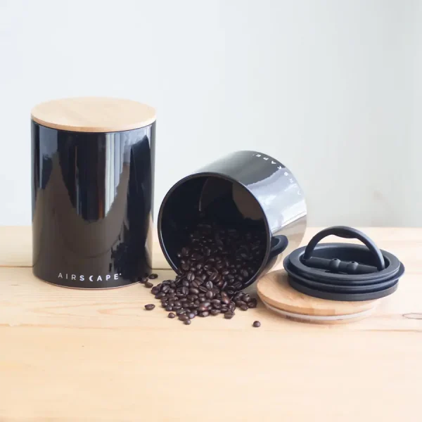 a large black ceramic canister and small coffee canister tipped over with coffee spilling out on a coffee table