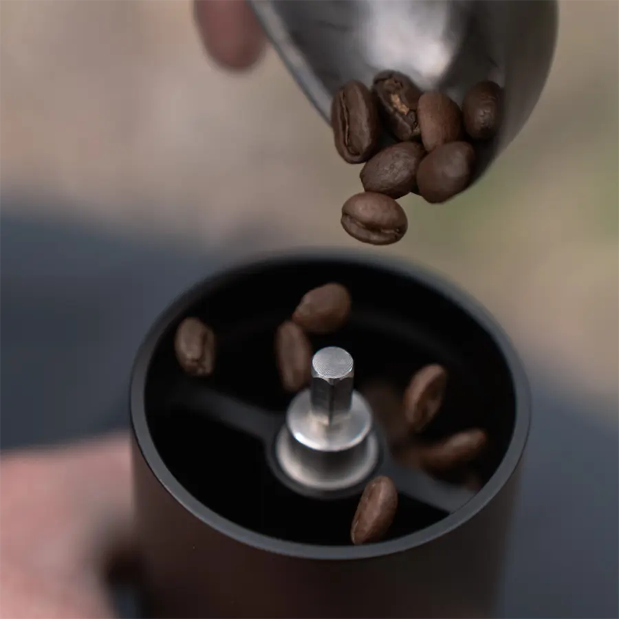person using coffee spoon to pour coffee beans into coffee grinder