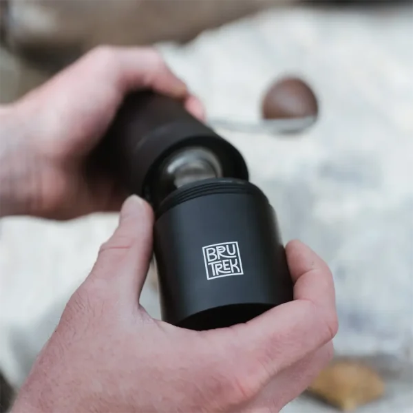 person taking reservoir off hand coffee grinder for coffee grounds