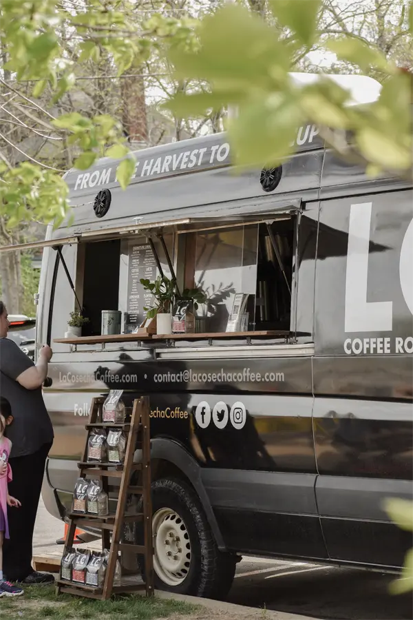 Person being served at farmers market by La Cosecha Coffee Van