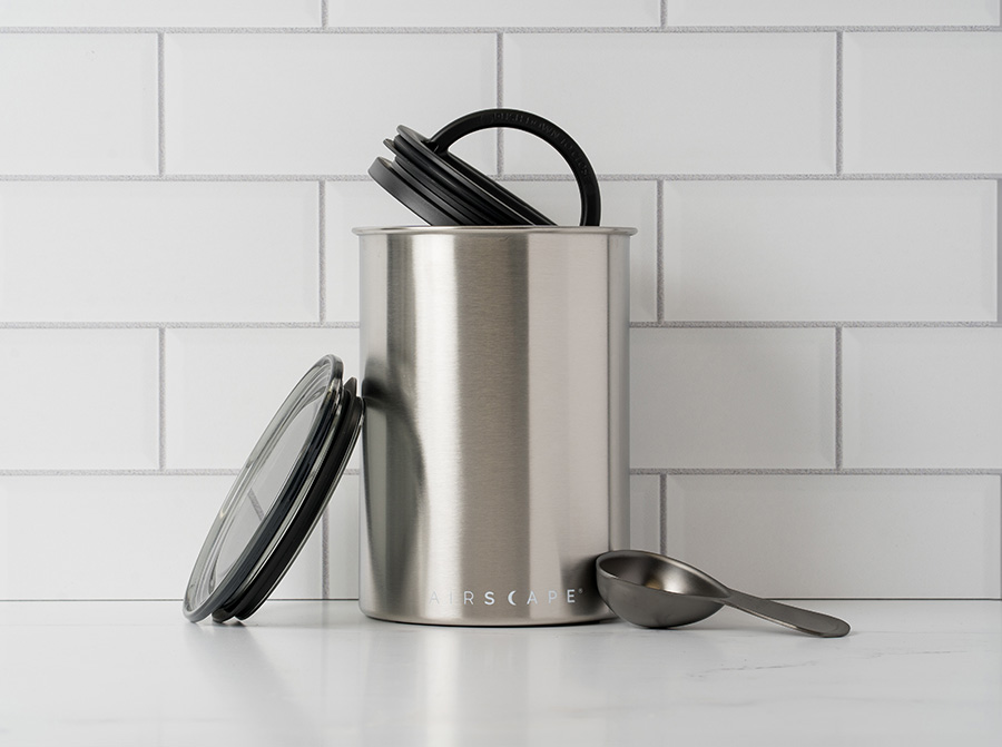 stainless steel airtight coffee storage container on a kitchen counter next to a coffee spoon